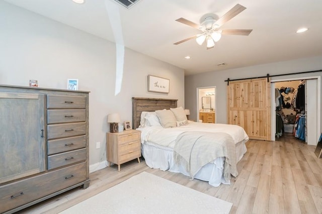 bedroom with recessed lighting, a barn door, connected bathroom, light wood finished floors, and baseboards