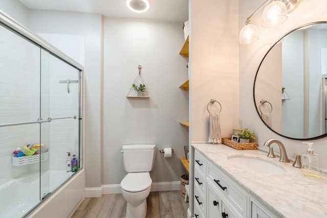 bathroom featuring baseboards, toilet, wood finished floors, enclosed tub / shower combo, and vanity