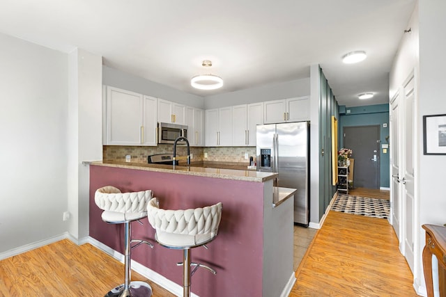 15 Freedom Way Unit 401, Jersey City, NJ 07305 - kitchen with stainless steel appliances, a kitchen bar, light wood-style flooring, backsplash, and white cabinetry