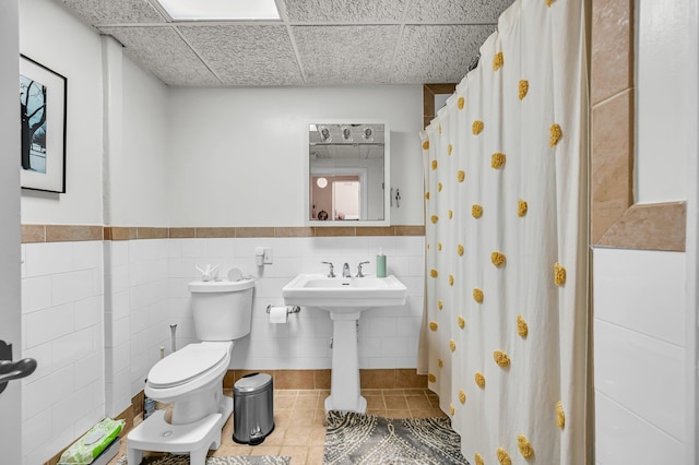 full bathroom with tile walls, toilet, wainscoting, a sink, and tile patterned flooring