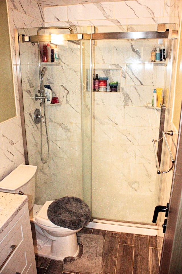 bathroom with walk in shower, vanity, tile walls, hardwood / wood-style floors, and toilet