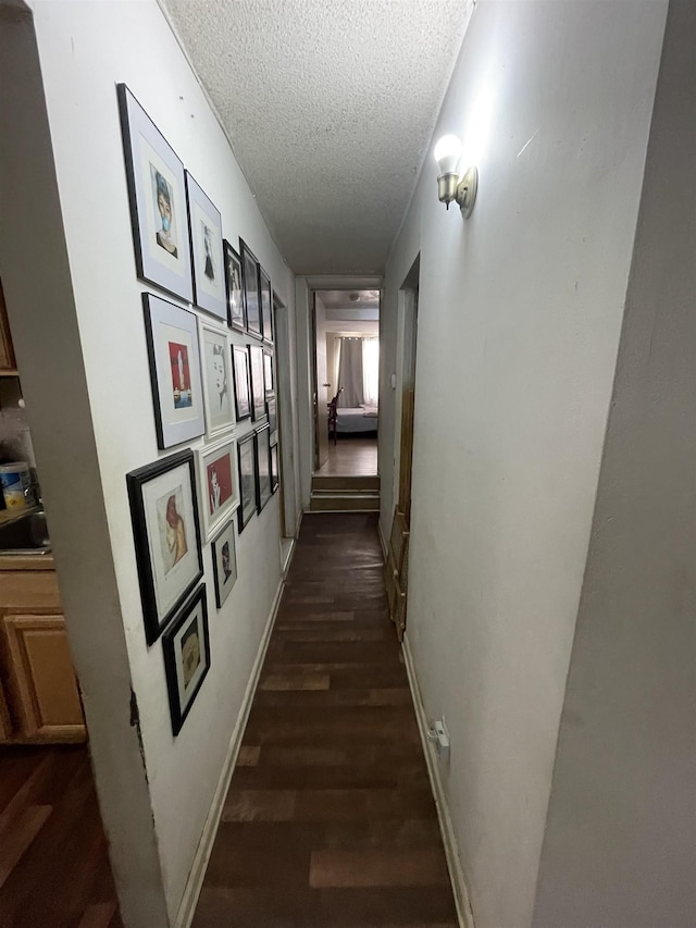 hall featuring dark wood-style floors, a textured ceiling, and baseboards