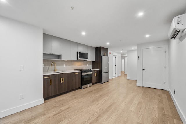 kitchen with light wood-style flooring, appliances with stainless steel finishes, light countertops, an AC wall unit, and a sink