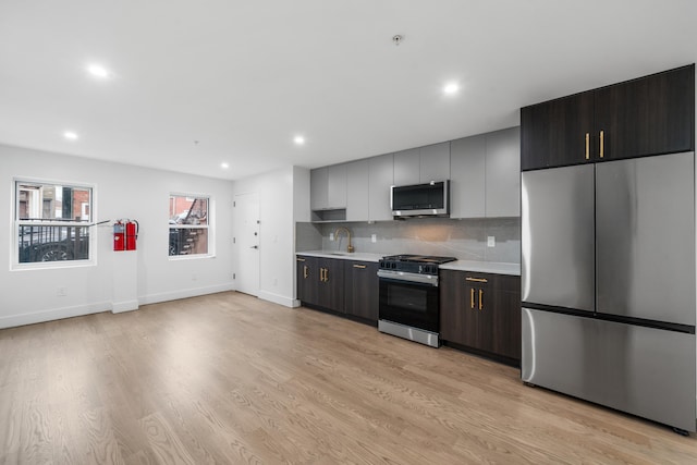 kitchen with sink, light hardwood / wood-style floors, tasteful backsplash, and appliances with stainless steel finishes