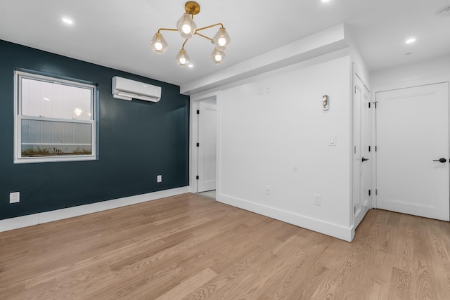 empty room with light wood-type flooring, a wall mounted AC, and an inviting chandelier