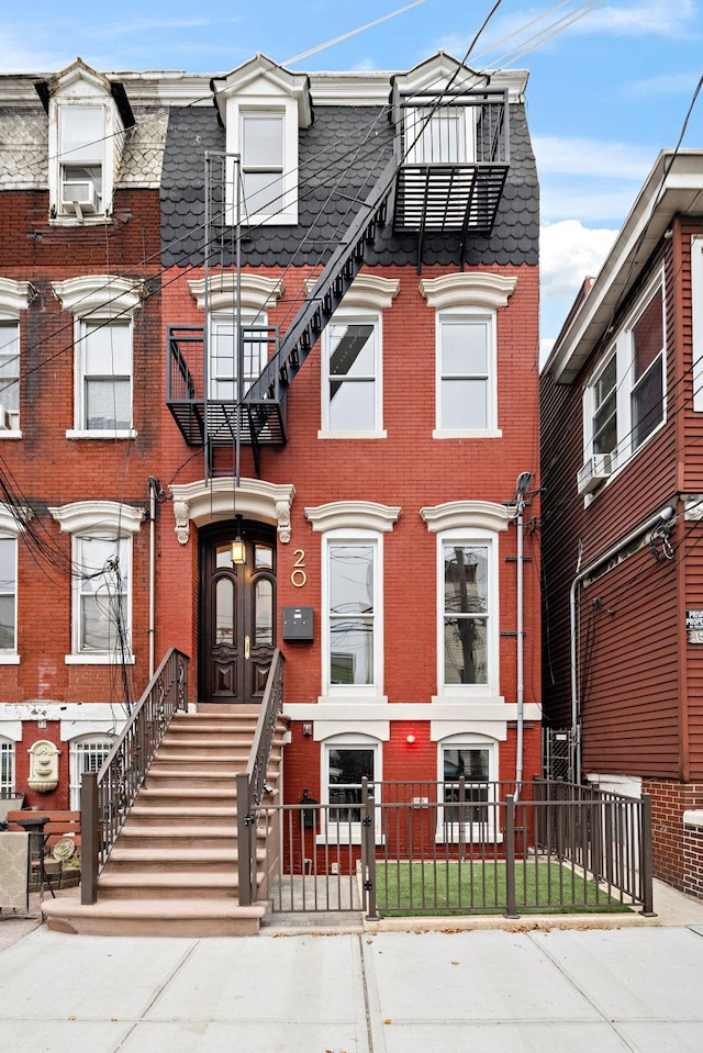 multi unit property with a fenced front yard, brick siding, and mansard roof