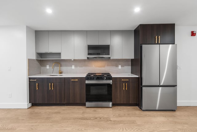 kitchen with light hardwood / wood-style floors, appliances with stainless steel finishes, sink, dark brown cabinetry, and backsplash