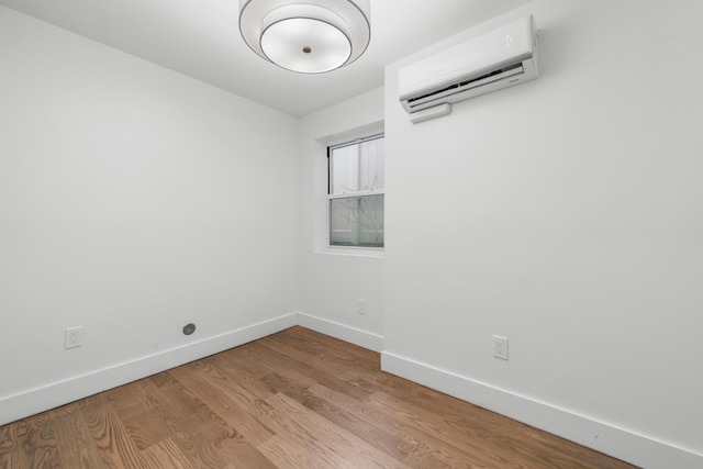 unfurnished room featuring baseboards, wood finished floors, and a wall mounted air conditioner