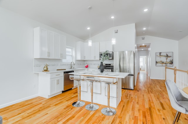 kitchen with stainless steel appliances, vaulted ceiling, decorative light fixtures, a center island, and white cabinetry