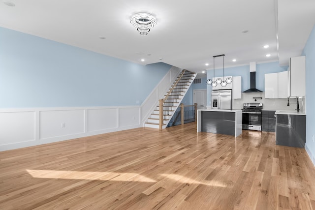 unfurnished living room featuring crown molding, light wood-type flooring, stairway, and a wainscoted wall