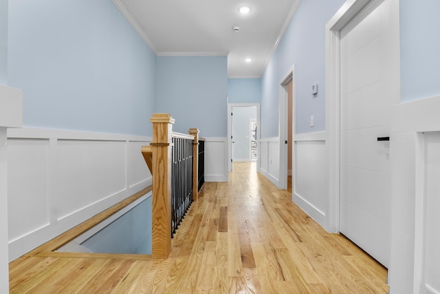 corridor featuring an upstairs landing, ornamental molding, light wood finished floors, and a wainscoted wall