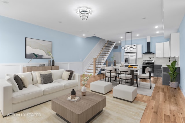 living area featuring wainscoting, stairs, light wood-style floors, a decorative wall, and recessed lighting