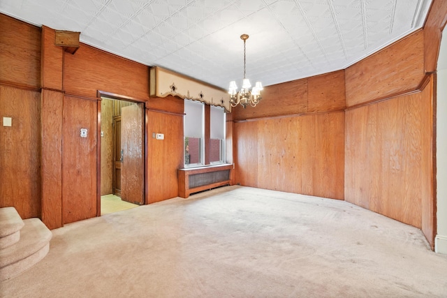 spare room with a notable chandelier, wood walls, and carpet flooring