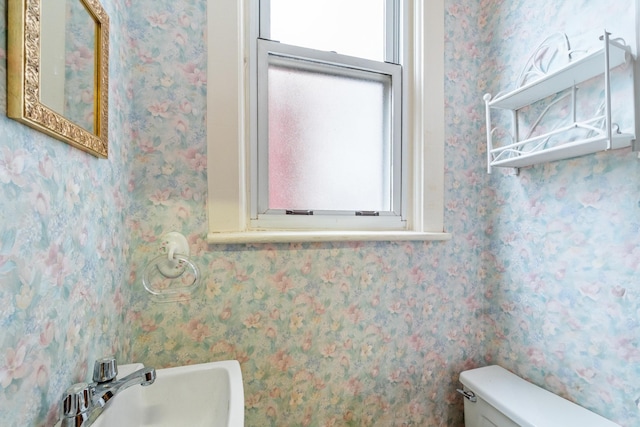 bathroom with a sink, toilet, and wallpapered walls