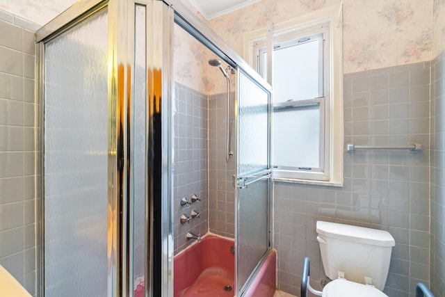 full bath with combined bath / shower with glass door, toilet, wallpapered walls, and tile walls