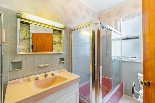 full bath with wallpapered walls, bath / shower combo with glass door, toilet, vanity, and tile walls