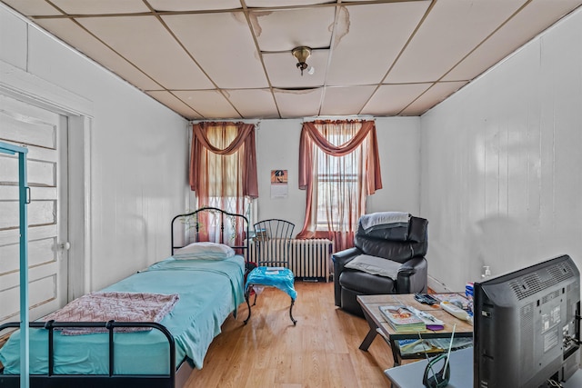 bedroom featuring radiator heating unit, light hardwood / wood-style flooring, and a drop ceiling