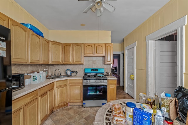 kitchen with black refrigerator, stainless steel gas range oven, ceiling fan, sink, and light brown cabinets