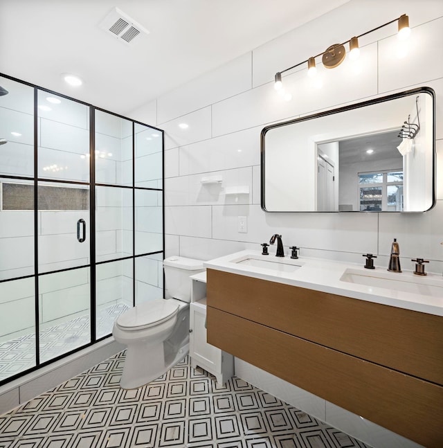 bathroom featuring vanity, toilet, a shower with shower door, and tile walls