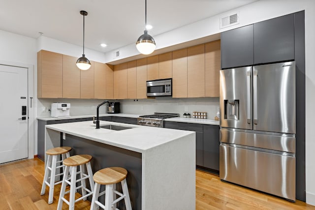 kitchen featuring sink, appliances with stainless steel finishes, decorative light fixtures, and a kitchen island with sink