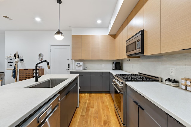 kitchen with decorative light fixtures, sink, backsplash, light hardwood / wood-style floors, and stainless steel appliances