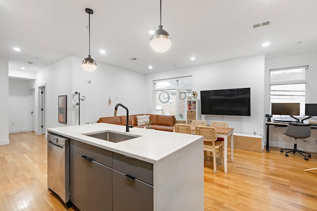 kitchen featuring decorative light fixtures, dishwasher, sink, a center island with sink, and light wood-type flooring