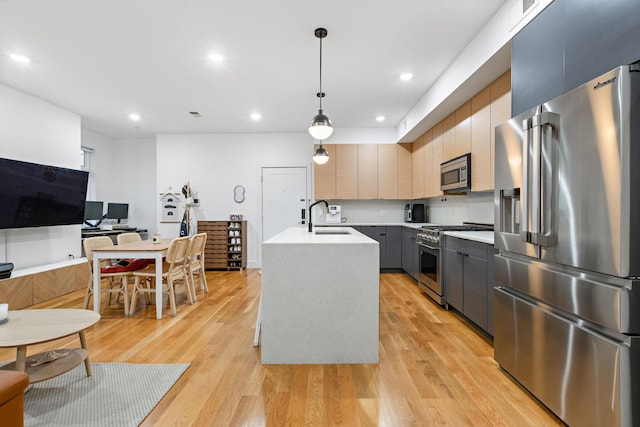 kitchen with gray cabinets, decorative light fixtures, sink, premium appliances, and a kitchen island with sink