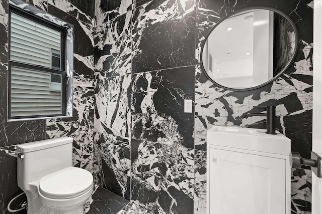 half bathroom featuring marble finish floor, vanity, toilet, and stone wall