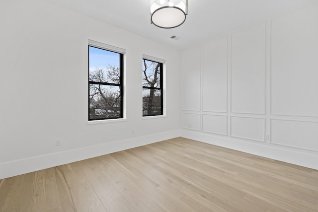 unfurnished room featuring light wood-type flooring, visible vents, a decorative wall, and baseboards