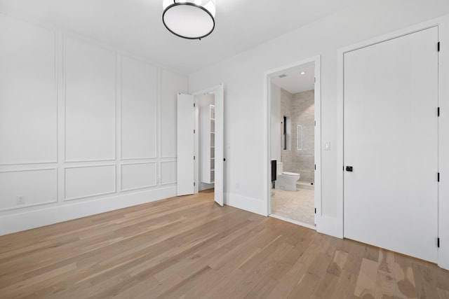 unfurnished bedroom featuring light wood-type flooring, ensuite bath, and a decorative wall