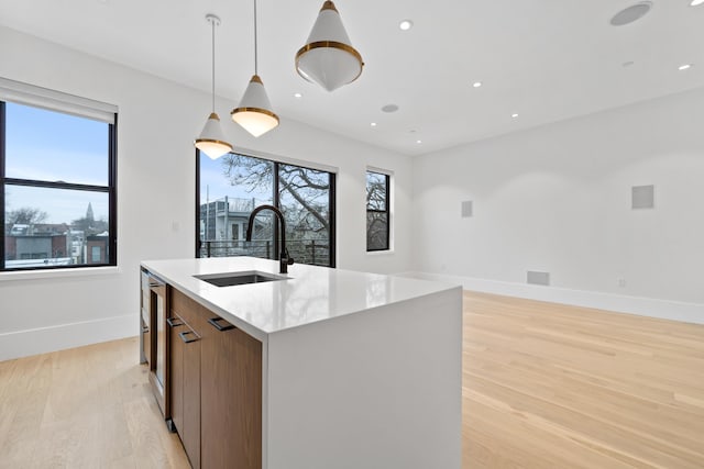 kitchen featuring light wood finished floors, an island with sink, open floor plan, hanging light fixtures, and a sink