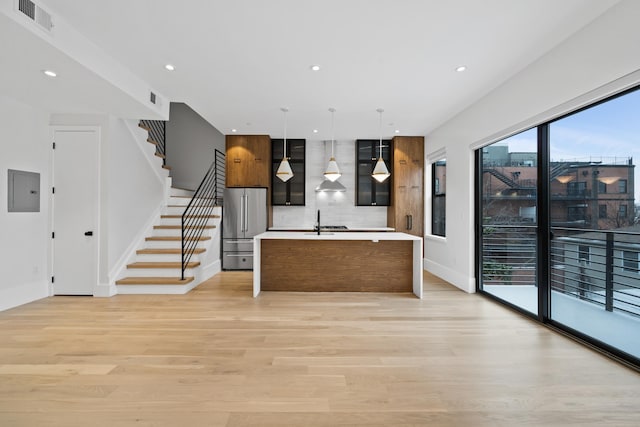 kitchen featuring an island with sink, light wood-style flooring, high quality fridge, and light countertops