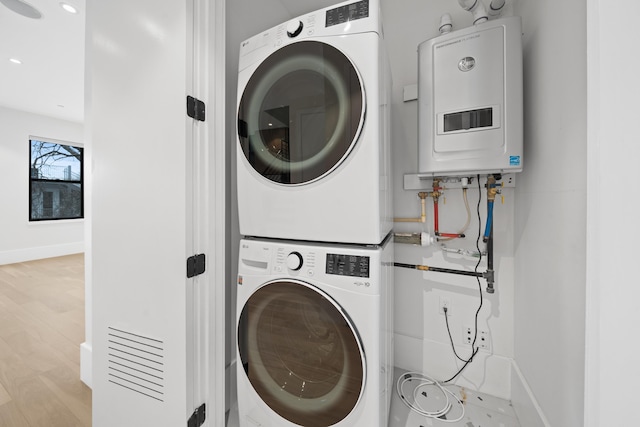 clothes washing area with laundry area, baseboards, stacked washer / drying machine, wood finished floors, and water heater