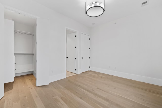 unfurnished bedroom featuring visible vents, baseboards, light wood-style flooring, a spacious closet, and a closet