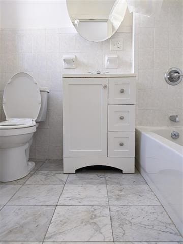 full bathroom featuring bathtub / shower combination, vanity, toilet, and tile walls