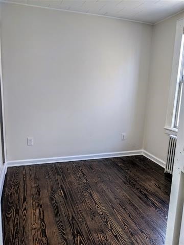 empty room with dark wood-type flooring and radiator