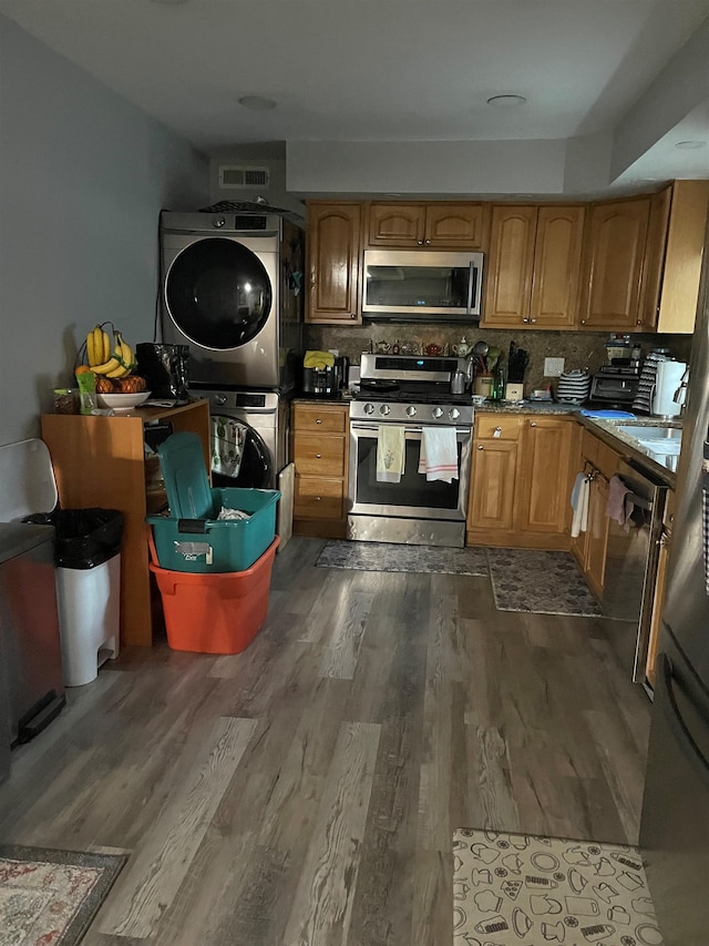 kitchen featuring dark wood-type flooring, stainless steel appliances, tasteful backsplash, and stacked washer and clothes dryer