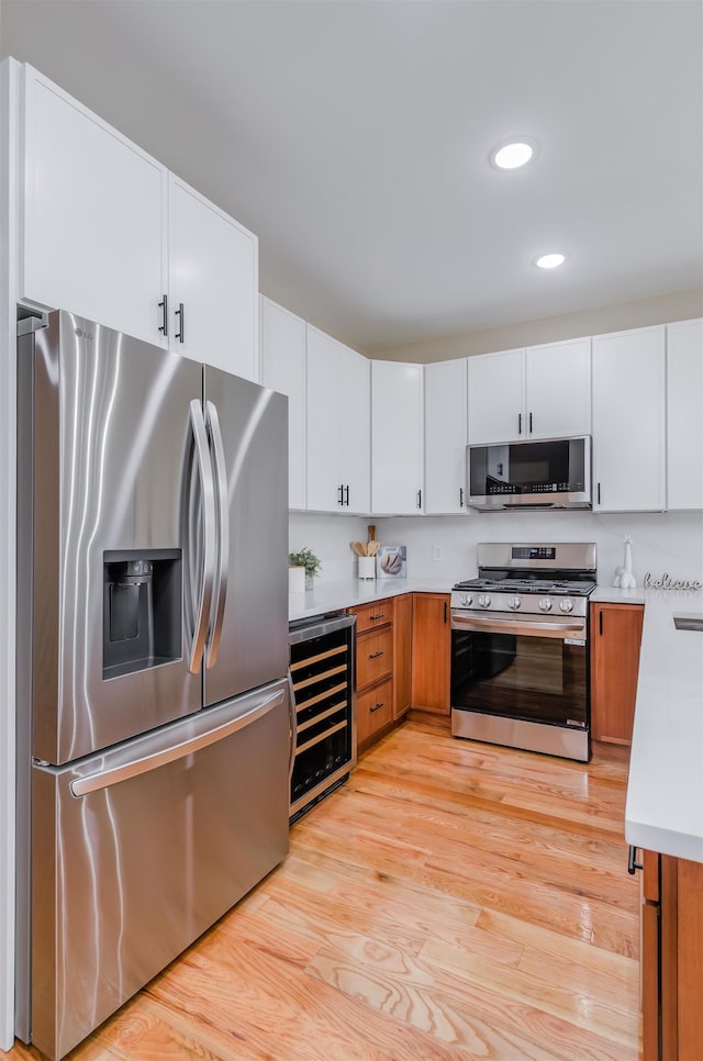 kitchen with light wood finished floors, stainless steel appliances, light countertops, white cabinetry, and beverage cooler