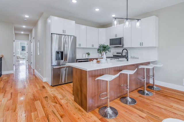 kitchen with appliances with stainless steel finishes, a peninsula, light countertops, light wood-type flooring, and a sink