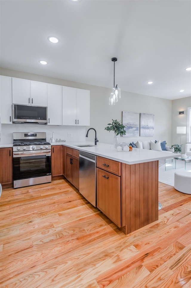 kitchen with a peninsula, a sink, open floor plan, light countertops, and appliances with stainless steel finishes