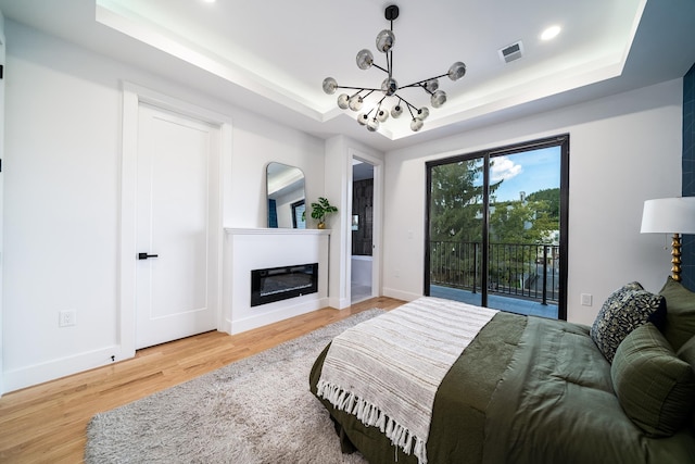 bedroom with wood finished floors, a raised ceiling, a glass covered fireplace, and access to exterior