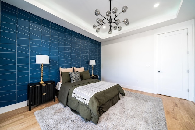 bedroom with light wood-type flooring, a tray ceiling, and an accent wall