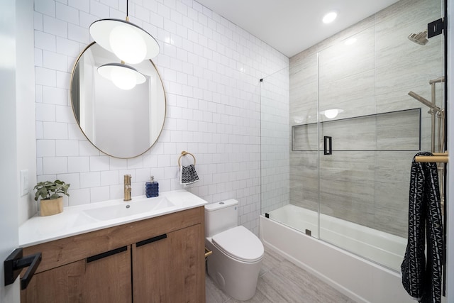 bathroom featuring vanity, tile walls, toilet, and bath / shower combo with glass door