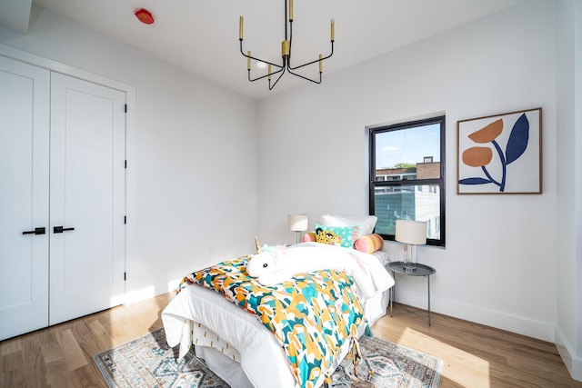 bedroom featuring a closet, a chandelier, baseboards, and wood finished floors