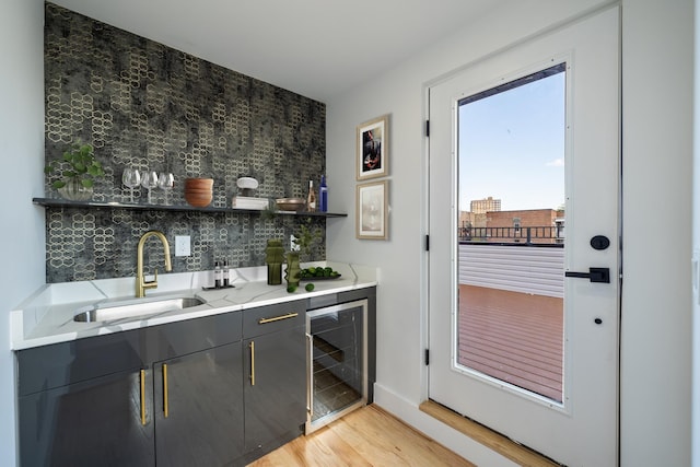 bar featuring beverage cooler, a sink, backsplash, light wood finished floors, and wet bar