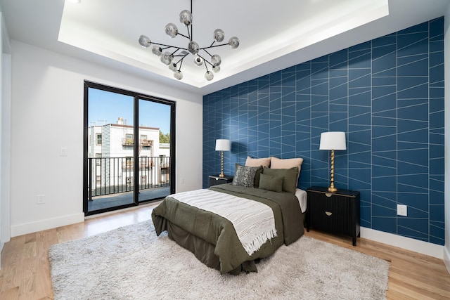 bedroom featuring wood finished floors, baseboards, a tray ceiling, access to exterior, and a notable chandelier