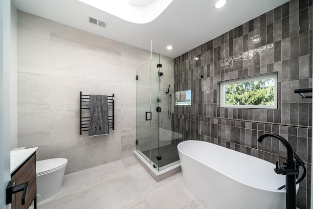 bathroom featuring vanity, visible vents, a freestanding bath, a shower stall, and tile walls