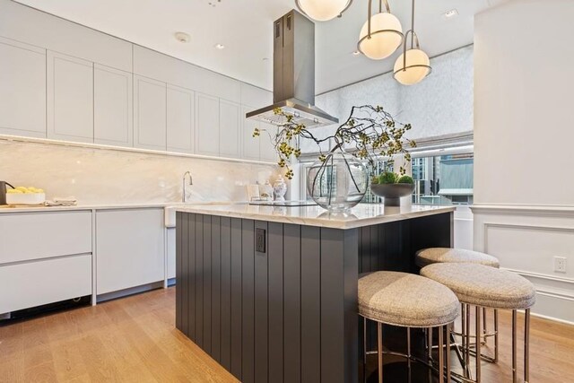 kitchen with decorative light fixtures, light wood-type flooring, white cabinetry, a center island, and island range hood