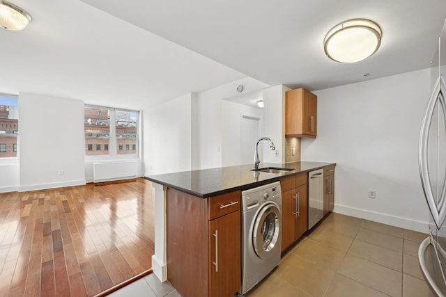 kitchen featuring washer / clothes dryer, stainless steel appliances, dark stone countertops, sink, and kitchen peninsula