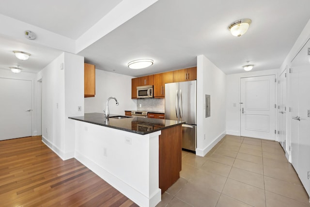 kitchen featuring kitchen peninsula, sink, electric panel, decorative backsplash, and stainless steel appliances